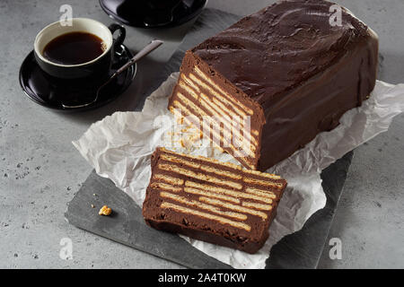 Cioccolato fondente Torta di biscotti Kalter Hund con una fetta tagliata, servita su grigio vassoio con due tazze di caffè, visto da vicino da un angolo alto su grigio ba Foto Stock