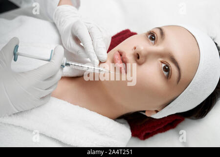 Vista da sopra delle mani di estetista in bianco guanti di gomma tenendo la siringa e rendendo iniezione di Botox labbra femmina. Bella giovane donna rece Foto Stock