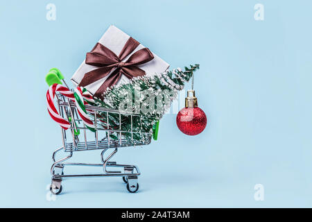 Albero di natale, confezione regalo e candy canes in miniatura carrello con pastello su sfondo blu con una copia dello spazio. Foto Stock
