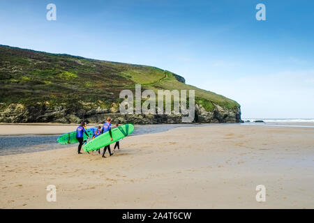 Un gruppo di surfers e loro istruttore che trasportano le loro tavole da surf su Mawgan Porth Beach a nord della costa della Cornovaglia. Foto Stock