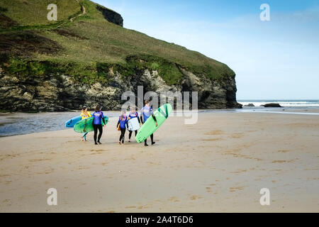 Un gruppo di surfers e loro istruttore che trasportano le loro tavole da surf su Mawgan Porth Beach a nord della costa della Cornovaglia. Foto Stock