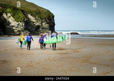 Un gruppo di surfers e loro istruttore che trasportano le loro tavole da surf su Mawgan Porth Beach a nord della costa della Cornovaglia. Foto Stock