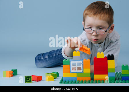 Lo zenzero piccolo ragazzo disteso sul pavimento, assemblaggio di casa da gioco di costruzioni isolati Foto Stock