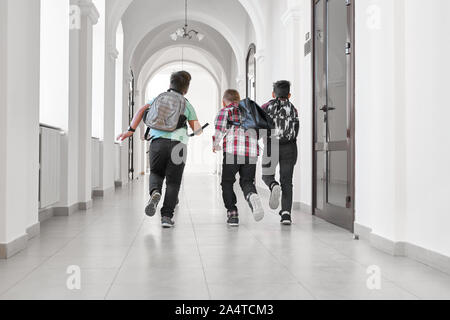 Gruppo di scolari con la scuola, zaini in esecuzione nei corridoi della scuola. I compagni di scuola divertendosi e in esecuzione nella pausa tra le lezioni o dopo le lezioni. Foto Stock