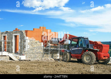 Costruzione di una pietra-placcati casa di mattoni usando una gru telescopica. Foto Stock