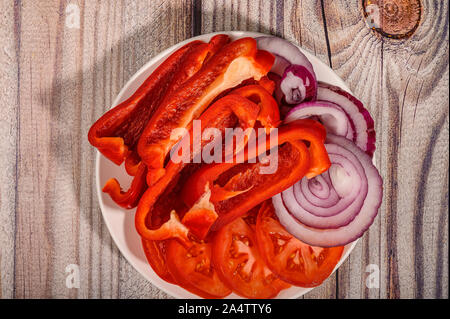 Pomodori a fette, i peperoni e le cipolle in una piastra su un tavolo di legno Foto Stock