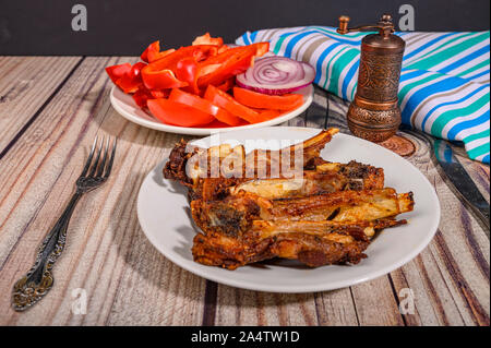Costolette di agnello marinato con spezie grigliato in una piastra sul tavolo. Con pomodori a fette, i peperoni e le cipolle Foto Stock