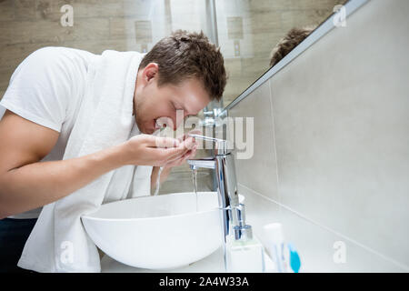 Giovane uomo bello sciacqua il viso con acqua in bagno Foto Stock