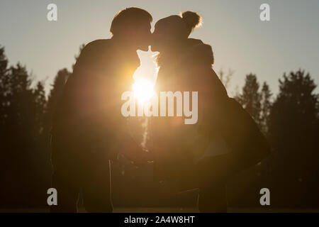 Donna incinta baciare il partner esterni visualizzati in silhouette con la sunflare. Foto Stock