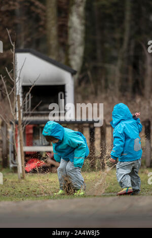 Due bambini indossare giacche blu a giocare all'aperto nella pozza. Foto Stock