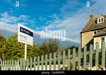 Agente immobiliare Hamptons in vendita segno esposto al di fuori del Cotswold cottage in pietra, Gloucestershire, Regno Unito Foto Stock