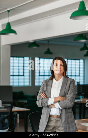 Fiducioso imprenditrice in piedi con le braccia incrociate in un ufficio Foto Stock