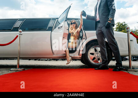 Autista aiutando vip donna o star fuori di limo sul tappeto rosso Foto Stock