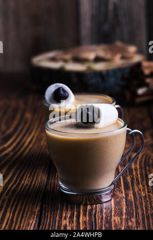Happy monster, pumpkin spice latte con panna montata e grandi occhi marshmallow sulla parte superiore, Halloween dessert, marshmallow faccina sorridente sul rustico scheda di legno Foto Stock