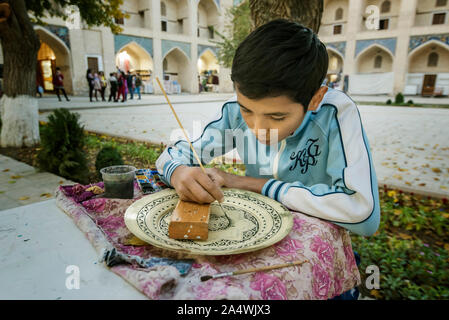 Un ragazzo dipinto una piastra. Nadir Divan Begi madrasa, oggi un centro per crafstmen. Bukhara, un sito Patrimonio Mondiale dell'UNESCO. Uzbekistan Foto Stock