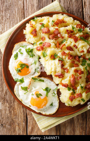 Spiced purè di patate con pancetta e prezzemolo e servite con uova fritte close-up su una piastra sul tavolo. Verticale in alto vista da sopra Foto Stock