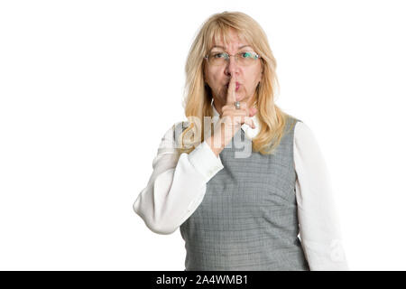È un gesto segreto. Una donna adulta in bicchieri detiene un dito vicino le labbra mentre in piedi su uno sfondo luminoso. Foto Stock