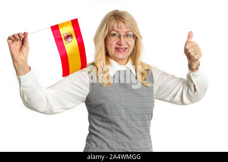 Felice donna matura con la bandiera della Spagna che mostra il pollice in alto, guardando avanti con la telecamera e isolato su sfondo bianco. Imparare lo spagnolo. Foto Stock