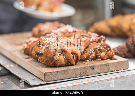 Twisted tradizionale svedese rotoli alla cannella presso una caffetteria. Le ciambelle dolci sono su un tagliere di legno. Foto Stock