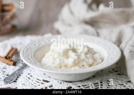 Una ciotola di in casa tradizionale budino di riso su un crochet fatti a mano tovaglia, su una tavola in legno rustico. Ci sono alcune stecche di cannella accanto al wh Foto Stock