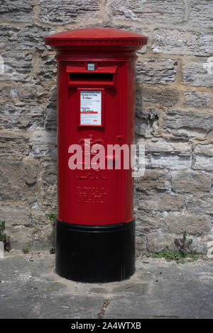 Royal Mail Post Box nero e rosso di fronte a un muro di pietra grigia, Ripon, North Yorkshire, Inghilterra, Regno Unito. Foto Stock