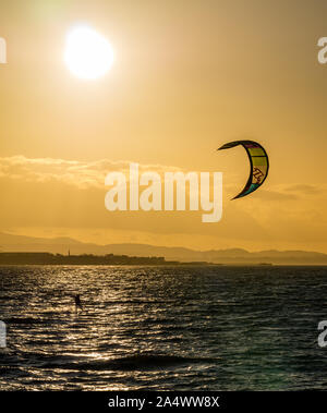 Longniddry Bents, East Lothian, Scozia, Regno Unito, 16 ottobre 2019. Regno Unito: Meteo un kite surfer gode il vento nelle ultime ore prima del tramonto con un bagliore arancione che illumina il cielo attraverso il Firth of Forth, guardando verso Edimburgo Foto Stock