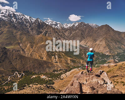 Bionda caucasica tourist girl su una escursione guardando verso la coperta di neve Alto Atlante monuntain picchi con Jebel Toubkal nel mezzo in Marocco Foto Stock