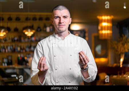 Giovani brutale bello cuoco capo in posa di lusso moderno ristorante interno. Foto Stock