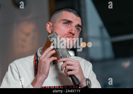 Bel giovane cuoco capo azienda coltello di rasatura e la barba e i peli nel moderno ristorante interno. Close up Foto Stock