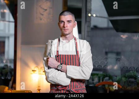 Giovane bello brutale cuoco capo azienda coltello nel moderno ristorante interno. Foto Stock