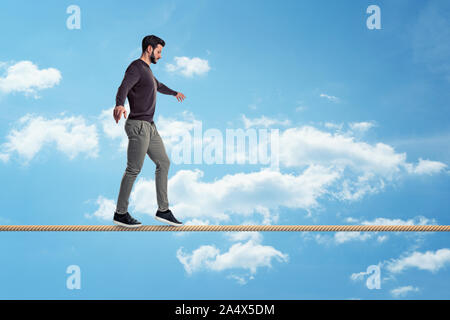 Un casualmente vestito con barba passeggiate attentamente su una corda su uno sfondo con cielo. Foto Stock