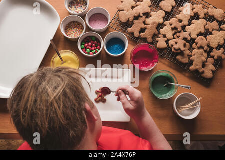 Ragazzo la decorazione di pan di zenzero con la glassa su una piastra Foto Stock