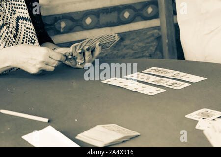 Tonalità seppia invecchiata effetto immagine di womans mano con unghie verniciate tenendo il gioco carte card durante il giorno in greco hill bar di paese. Foto Stock