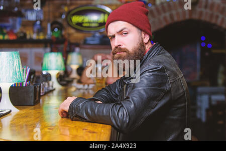 Brutale lonely hipster. Brutale parigamba uomo barbuto sedersi al banco bar. Venerdì sera. Hipster rilassante presso il bar. Il bar è un luogo rilassante per avere bere e rilassarsi. Uomo con barba trascorrere il tempo libero nella barra di colore scuro. Foto Stock