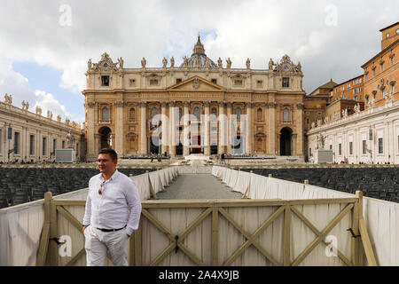 Turismo a maschio in posa per fotocamera in Piazza San Pietro con la Basilica di San Pietro sullo sfondo nello Stato della Città del Vaticano Foto Stock