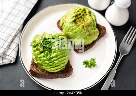 Avocado toast sulla piastra bianca. Fette di avocado su pane di segale. Una sana prima colazione, snack o antipasto vegetariano vegano cibo Foto Stock
