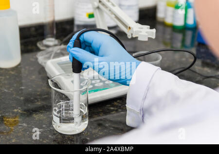 Donna mani di eseguire test pH sul misuratore di pH dello strumento elettronico per il controllo della qualità nell'industria chimica. Foto Stock