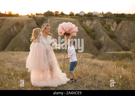 Elegante ragazzo dà un grande fiore a sua madre in un campo al tramonto. Foto Stock