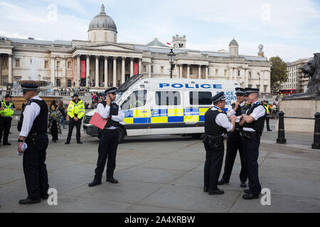 Londra, Regno Unito. 16 ottobre, 2019. Gli agenti di polizia e veicoli parcheggiati su Trafalgar Square vicino a centinaia di attivisti del clima dalla ribellione di estinzione sfidando la Metropolitan Police divieto di estinzione della ribellione autunno Uprising proteste in tutta Londra sotto la sezione 14 dell ordine pubblico Act 1986 partecipando a un diritto di protestare di assemblaggio. La Metropolitan Police realizzati arresti, anche Partito Verde co-leader Jonathan Bartley e custode giornalista George Monbiot, dopo che un gruppo di manifestanti si sedette in strada in Whitehall. Credito: Mark Kerrison/Alamy Live News Foto Stock