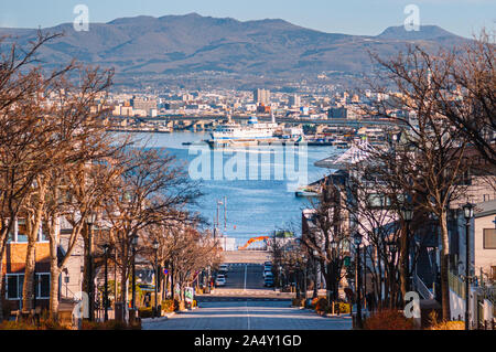 Dicembre 2, 2018 Hakodate, Giappone - Motomachi pendenza strada con albero sfrondato lungo entrambi i lati con Hakodate bay view in background con cielo blu Foto Stock