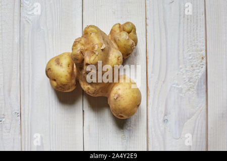 Brutto potato isolato su bianco sullo sfondo di legno. Foto Stock