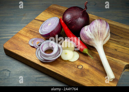 Cipolla rossa, intero e affettato in anelli, aglio e peperoncino verdure, seduta sul tagliere di legno e visualizzare in primo piano, da un angolo alto Foto Stock