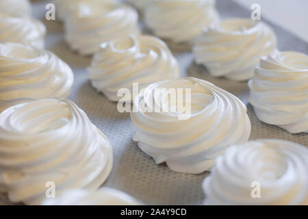 Preparazione di un bianco torta di meringa Pavlova. Meringa volute su sfondo bianco Foto Stock