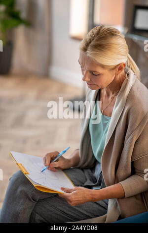 Bionda psicanalista indossando Elegante cardigan rendendo note Foto Stock