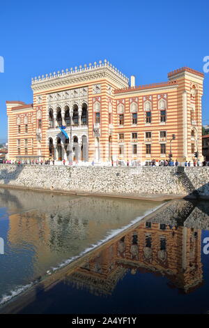 SARAJEVO, BOSNIA ERZEGOVINA - 15 settembre 2019: il colorato Vijecnica (ex National Library e Municipio) riflesso nel fiume Miljacka Foto Stock