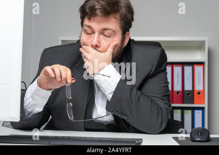Imprenditore in ufficio con il mal di testa si appoggia sul tavolo Foto Stock