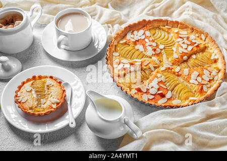 Close-up di Francese Crostata di pere, la Tarte Bourdaloue riempito con pere in camicia e frangipane crema servita su una tavola di cemento con una tazza di bevanda di cacao Foto Stock