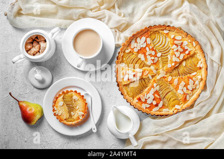 Francese Crostata di pere, la Tarte Bourdaloue riempito con pere in camicia e frangipane crema servita su una tavola di cemento con una tazza di cacao drink freschi e c Foto Stock