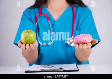 Uno stile di vita sano, cibo e sport concept. Una sana versus malsano. Medico donna mano azienda ciambella e mela verde. Foto Stock