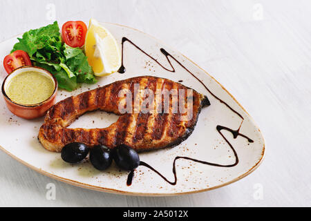 Salmone alla griglia bistecca, serviti con salsa di limone, lattuga e pomodoro, su un piatto bianco. Copyspace. Foto Stock